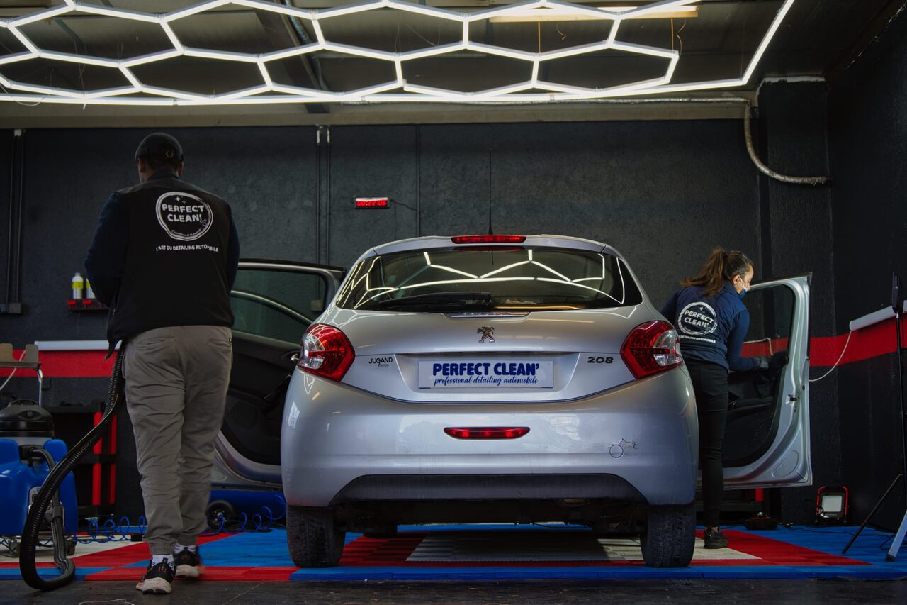 L'atelier Perfect Clean 74 à Cranves-Sales : deux détailleurs au travail sous l'éclairage hexagonal LED, autour d'une Peugeot 208 en cours de prestation
